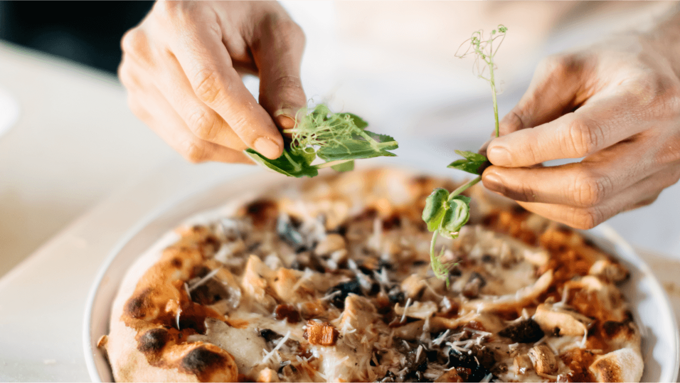 Mushroom and pancetta pizza, a man places green herbs ontop.