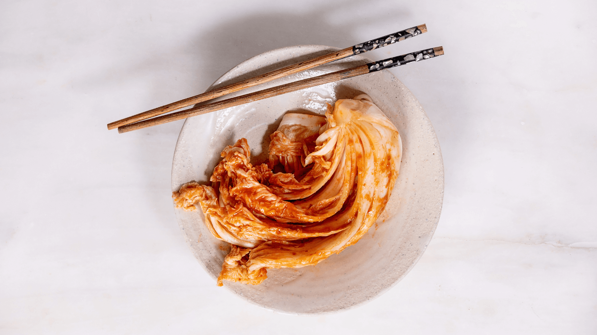 Kimchi in a white bowl with chopsticks.