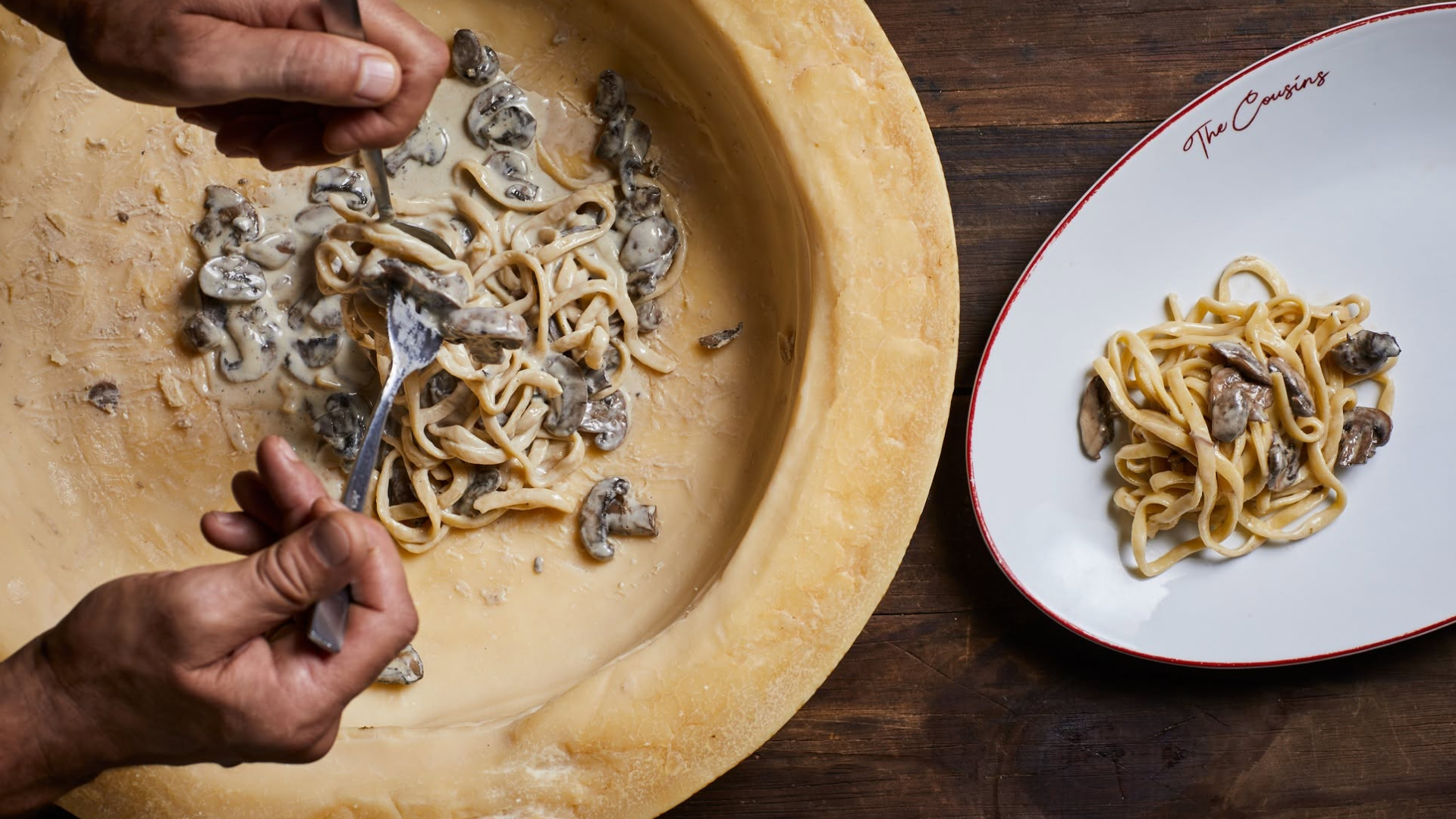 Grana Padano cheese wheel with a serving of mushroom pasta on a clean white plate