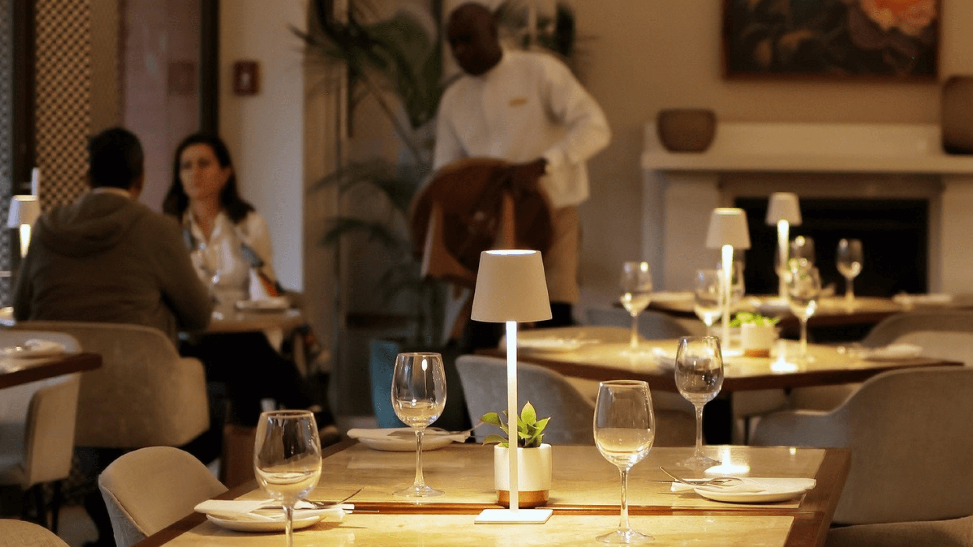 A table setting with guests at the back and a server helping at Aduna Bistro