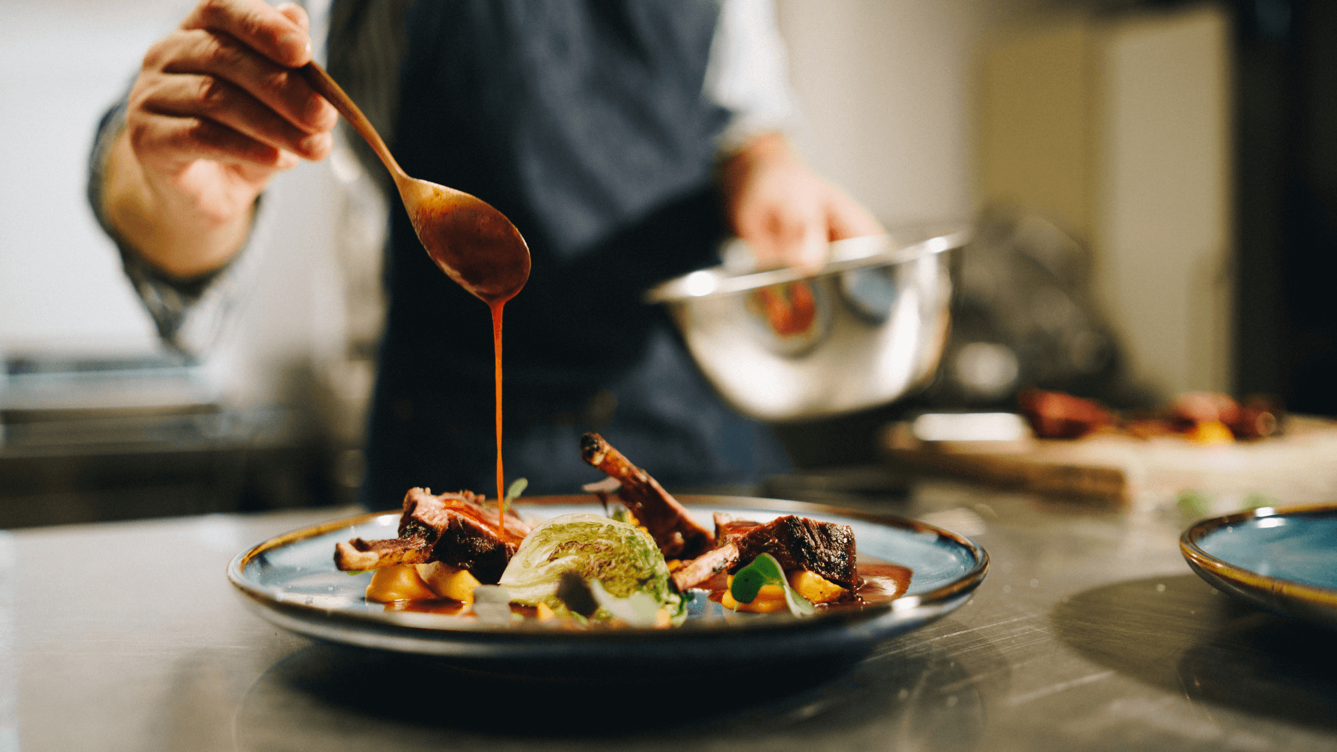 Plates and possibilities A chef pours sauce over a plate in the kitchen.