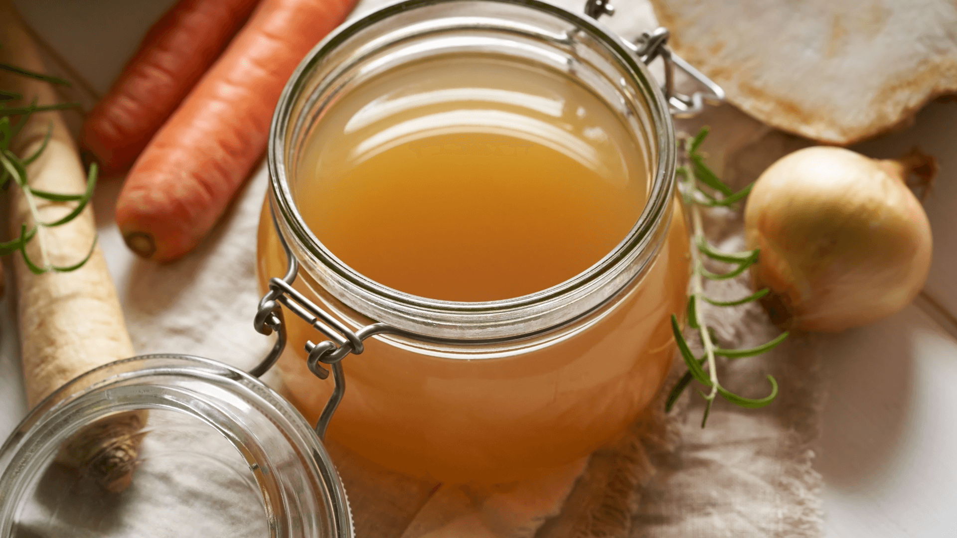 Quick luxe lunches: Simple ideas for weekday meals. Bone broth in a jar, next to carrots and onions. Bone broth can be used to make an easy, simple, but luxe lunch, perfect for any day of the week.