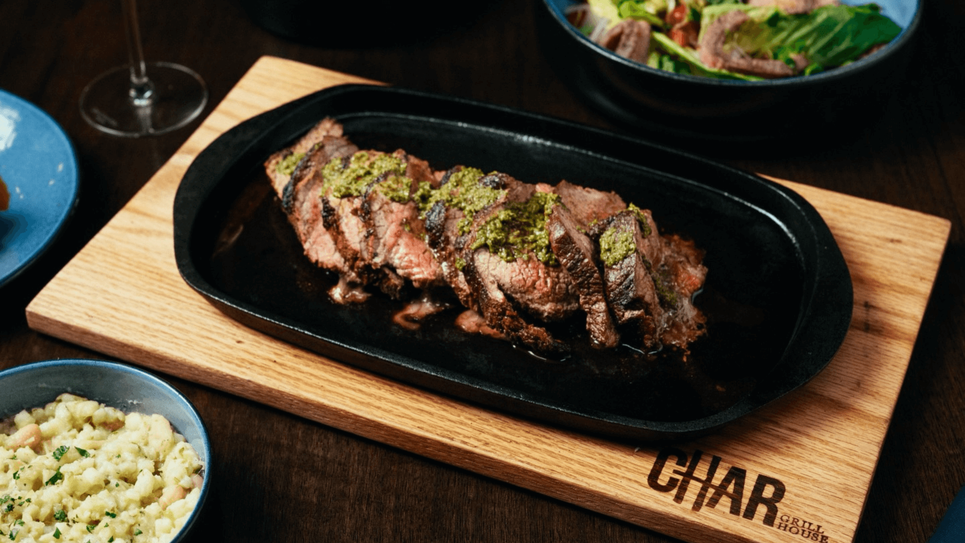 A cut piece of steak with green chimichurri sauce is placed on a black dish, which is on top of a wooden board.